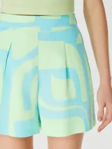 Short de tiro alto con diseño estampado geométrico en tonos verde y turquesa, cuenta con bolsillos laterales y cierre frontal.