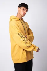 Canguro oversize color amarillo, con capucha y cordones ajustables con logo estampado. Presenta un bolsillo frontal tipo canguro y estampados gráficos en las mangas.