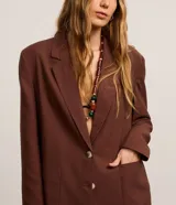 Blazer oversized de Marfinno color marrón, confeccionado en mezcla de viscosa, poliéster y lino. Presenta solapas clásicas en el cuello, cierre frontal abotonado y bolsillos delanteros.