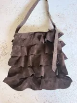 Cartera de hombro confeccionada artesanalmente en cuero gamuzado color marrón, con diseño de múltiples volados horizontales y correa ajustable con hebilla metálica.