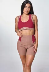 Conjunto deportivo de dos piezas compuesto por un top y un short de tiro alto. El top es de estilo deportivo con doble bretel y diseño bicolor en tonos bordó y marrón, con el logo 'bk.' estampado en el frente. El short es de corte ajustado, con diseño acanalado y paneles laterales en contraste de color bordó.