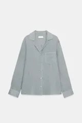 Camisa de lino con cuello solapa, manga larga con puños y cierre frontal con botones. Presenta un bolsillo de plastrón en el delantero.