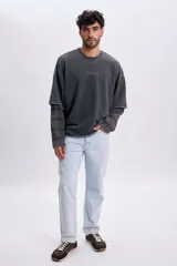 Sudadera gris oscuro de doble manga, con efecto de capas que simula una camisa a cuadros debajo, cuello redondo y bordado sutil en el pecho.