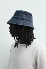 Sombrero tipo bucket de algodón con efecto lavado, color azul oscuro, con bordado frontal en tono amarillo que incluye la inscripción "Early Reggae Rub-A-Dub Sound". Cuenta con ala ancha con pespuntes decorativos.