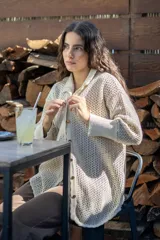 Camisa tejida en punto calado de algodón con destellos de lurex. Presenta una silueta oversize, mangas 3/4 ligeramente abullonadas, cuello camisero clásico y cierre frontal con botones metálicos.