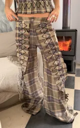 Pantalón de corte amplio con estampado de cuadros escoceses en tonos azul y verde. Presenta apliques de tela plisada con costuras decorativas en zigzag a lo largo de las piernas, tajos laterales y bolsillos funcionales.