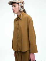 Camisa oversize de lyocell color tostado, con cuello clásico, cierre frontal de botones y mangas largas con puños anchos. Presenta un diseño de corte relajado con caída fluida.