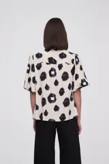 Blusa de manga corta con estampado de manchas negras y azules sobre fondo crema, cuello mao y cierre frontal con botones.