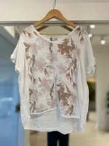 Blusa blanca de lino con escote redondo, manga corta con vuelta y estampa floral en tonos marrones y rosados en el frente.