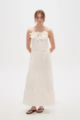 Vestido largo de algodón color blanco, con tirantes finos ajustables con lazos en los hombros, escote recto decorado con apliques florales tridimensionales, cordón ajustable en la cintura y falda larga con volados horizontales.