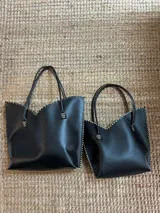 Cartera de cuero mediana con manijas largas, diseño con borde superior en corte en V y terminación artesanal con costuras contrastantes.