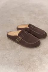 Zueco de cuero gamuzado color marrón, con diseño minimalista y elegante. Cuenta con una tira lateral con hebilla metálica regulable y plantilla acolchada. Su base es liviana y flexible.