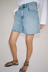 Shorts denim de tiro alto y corte relaxed, confeccionados en tejido vaquero celeste claro. Presentan trabillas en la cintura, diseño de cinco bolsillos, pliegues frontales y cierre con cremallera y botón metálico.