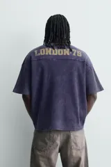 Remera de manga corta con corte relajado, confeccionada en tejido de algodón con textura tipo waffle. Presenta un efecto de lavado desgastado en color azul oscuro y estampado gráfico a contraste en el frente.