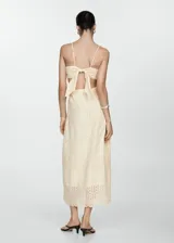Vestido midi de algodón en color beige, con diseño evasé, escote cuadrado y tirantes finos. Presenta detalles de tejido bordado tipo broderie, aberturas laterales cut-out en la cintura y cierre lateral con cremallera.