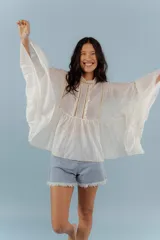 Camisa de algodón con diseño romántico, mangas amplias y detalles de puntillas verticales en el frente. Presenta un corte holgado y fluido.