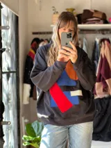 Buzo oversize negro con diseño artesanal de figuras geométricas aplicadas en tela de colores azul, naranja, rojo y blanco.