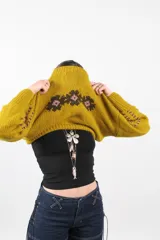 Sweater tejido de lana merino color mostaza, de corte boxy, con cuello redondo y diseño de flores bordadas en el pecho.
