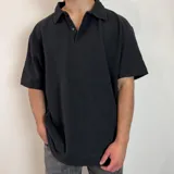 Chomba negra de corte oversize con cuello polo y tapeta de dos botones. Tejido de punto acanalado vertical.
