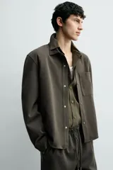 Sobrecamisa de corte regular fit en tejido elástico y transpirable, con cuello solapa, cierre frontal mediante botones a presión y bolsillo de plastrón en el pecho. Presenta mangas largas con puños abotonados y bajo con aberturas laterales.