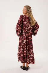 Vestido midi de silueta relajada con estampado animal print en tonos bordó y beige. Presenta escote redondo con abertura y lazos finos, mangas largas tipo globo con puños fruncidos y falda amplia con recortes horizontales.