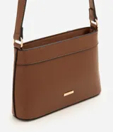 Cartera bandolera Satinato de color marrón, confeccionada en material sintético de poliuretano, con diseño pequeño, cierre de cremallera, asa larga ajustable y detalle de placa metálica dorada con el logotipo de la marca.