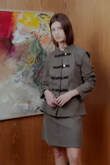 Chaqueta militar color verde oliva con cuello mao, cierre frontal con pasamanería y botones metálicos plateados.