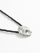 Collar con cordón negro y dije circular dorado con textura irregular.