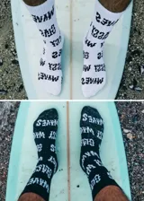 Pack de dos pares de medias de caña media, un par blanco con letras negras y otro par negro con letras blancas. Ambos pares tienen la palabra 'WAVES' estampada.