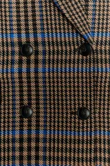 Abrigo largo de corte oversize con estampado de cuadros en tonos marrones y líneas azules. Presenta cuello de solapa, cierre frontal cruzado con botones, mangas largas y bolsillos delanteros con solapa.