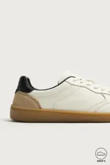 Zapatillas deportivas barefoot de hombre elaboradas en piel. Diseño en color blanco con detalles en negro y beige en el talón, y suela plana de goma marrón.