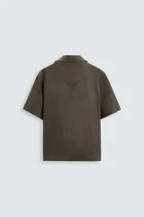 Camisa de lino color negro con calce relajado, cuello bowling y manga corta. Presenta cierre frontal con botones a tono y aberturas laterales en el bajo.