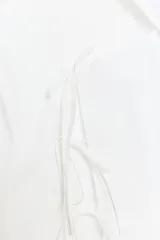 Camisa entallada de color blanco con cuello redondo, manga corta y abertura frontal. Presenta cierre con botones ocultos y detalle de lazadas en el frente.