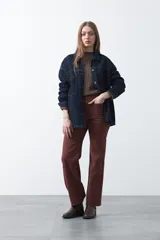 Pantalón de fit recto color marrón rojizo, confeccionado en cotton spandex, con costuras visibles que recorren la pierna y bordados decorativos. El ruedo del pantalón tiene un borde festoneado.