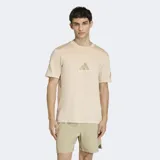 Remera de algodón color beige con cuello redondo y mangas cortas. Presenta el logo de Adidas estampado en el centro del pecho en un tono más oscuro y detalles gráficos en las mangas.