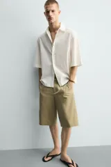Camisa de corte relajado y boxy fit, confeccionada en tejido con textura irregular. Presenta cuello solapa, manga corta y cierre frontal con botones.
