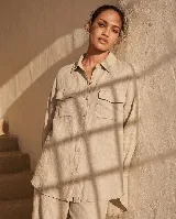 Camisa de lino de manga larga color beige, con botones frontales, cuello clásico y dos bolsillos con solapa en el pecho. Diseño holgado con bajo asimétrico, más largo en la parte trasera.