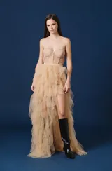 Falda larga de tul con diseño asimétrico, presentando una base corta y una sobrecapa voluminosa de volados en cascada que se extiende hacia atrás. Posee una cintura definida y un acabado etéreo.