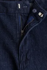 Pantalón de jean azul oscuro, tiro alto, con corte ajustado hasta la rodilla y pierna acampanada (bootcut). Presenta cierre frontal con botón y corchete ocultos, bolsillos al bies y bolsillos decorativos traseros.