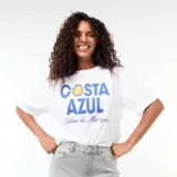 Remera oversize blanca de manga corta, con estampa frontal en tonos azules y amarillos con el texto "COSTA AZUL Palma de Majorque".