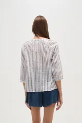 Camisa de algodón con diseño de rayas verticales y detalles bordados. Presenta cuello en V, cierre frontal con botones y mangas tres cuartos con terminación elástica.