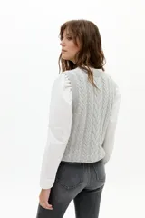 Chaleco de punto color gris melange, con cuello redondo, sisa amplia y largo a la cadera. Presenta un diseño de ochos tradicionales.