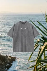 Remerón de corte oversize en color gris con efecto lavado (wash), cuello redondo y estampa frontal con la inscripción "GLASSY WAVES" en color blanco.