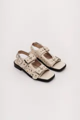 Sandalias negras de cuero con suela plana, dos tiras anchas con hebillas doradas y apliques metálicos.