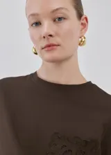 Remera marrón de corte recto, con cuello redondo, manga corta y detalle de bolsillo con bordado en el pecho.