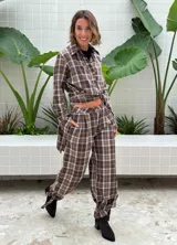 Pantalón de tiro alto con diseño a cuadros en tonos marrón y blanco. Presenta pinzas en la cintura, corte holgado y detalle de ajuste con trabilla en los tobillos.