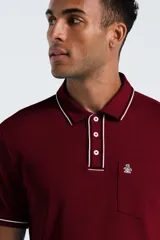 Chomba de manga corta color bordó con detalles de líneas blancas en el cuello y los puños. Presenta cierre frontal de tres botones y un bolsillo pequeño en el pecho con el logo de la marca bordado.