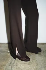 Pantalón de tiro alto con raya planchada en el delantero, corte flare con aberturas en el bajo y cierre lateral con cremallera oculta.