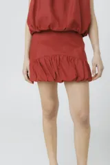 Falda corta color rojo óxido, con cintura alta y ruedo con efecto globo o fruncido voluminoso.