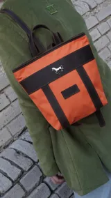 Mochila pequeña color borgoña con detalles en cuero marrón y aplique metálico de un caballo. Tiene manija superior y correas traseras regulables.